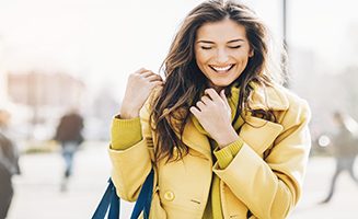 Beautiful young woman smiling and walking outdoors in the city, with sunlight and copy space